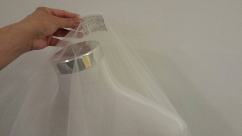 May include: A white tulle veil with a comb attached to the top edge. The veil is draped over a mannequin head.