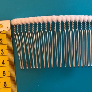 May include: A silver hair comb with white cotton padding on the top. The comb is 6 inches long and has a row of 18 teeth.