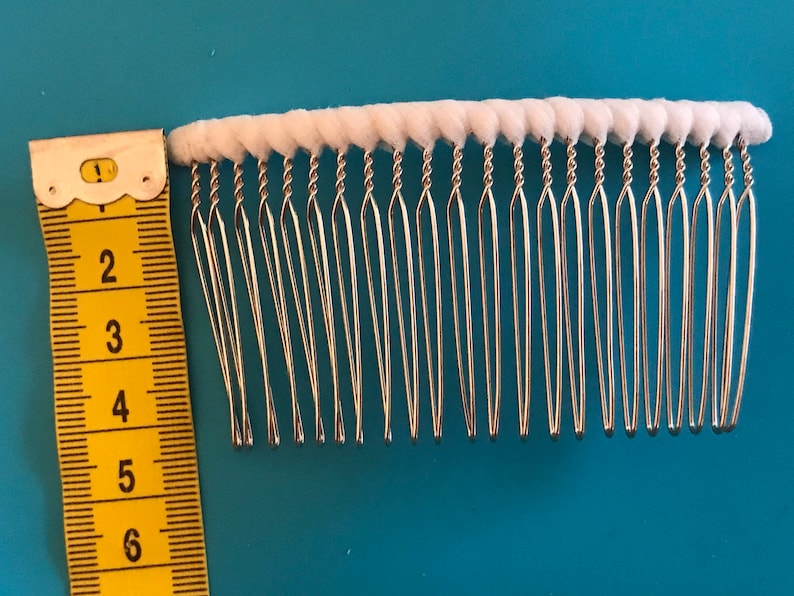May include: A silver hair comb with white cotton padding on the top. The comb is 6 inches long and has a row of 18 teeth.