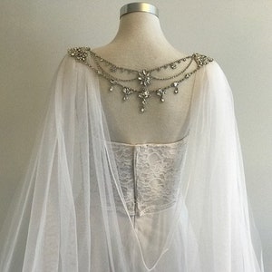 May include: A white tulle bridal cape with a crystal and rhinestone embellishment on the back.