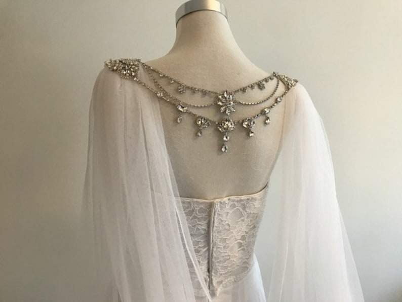 May include: White tulle bridal cape with a crystal and silver beaded embellishment on the back.