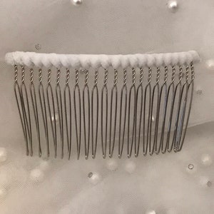 May include: A silver hair comb with a white padded base. The comb has a twisted wire design and is ideal for securing hair.
