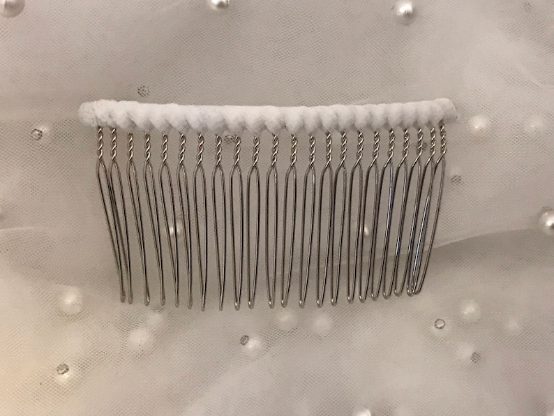 May include: A silver hair comb with a white padded base. The comb has a twisted wire design and is ideal for securing hair.