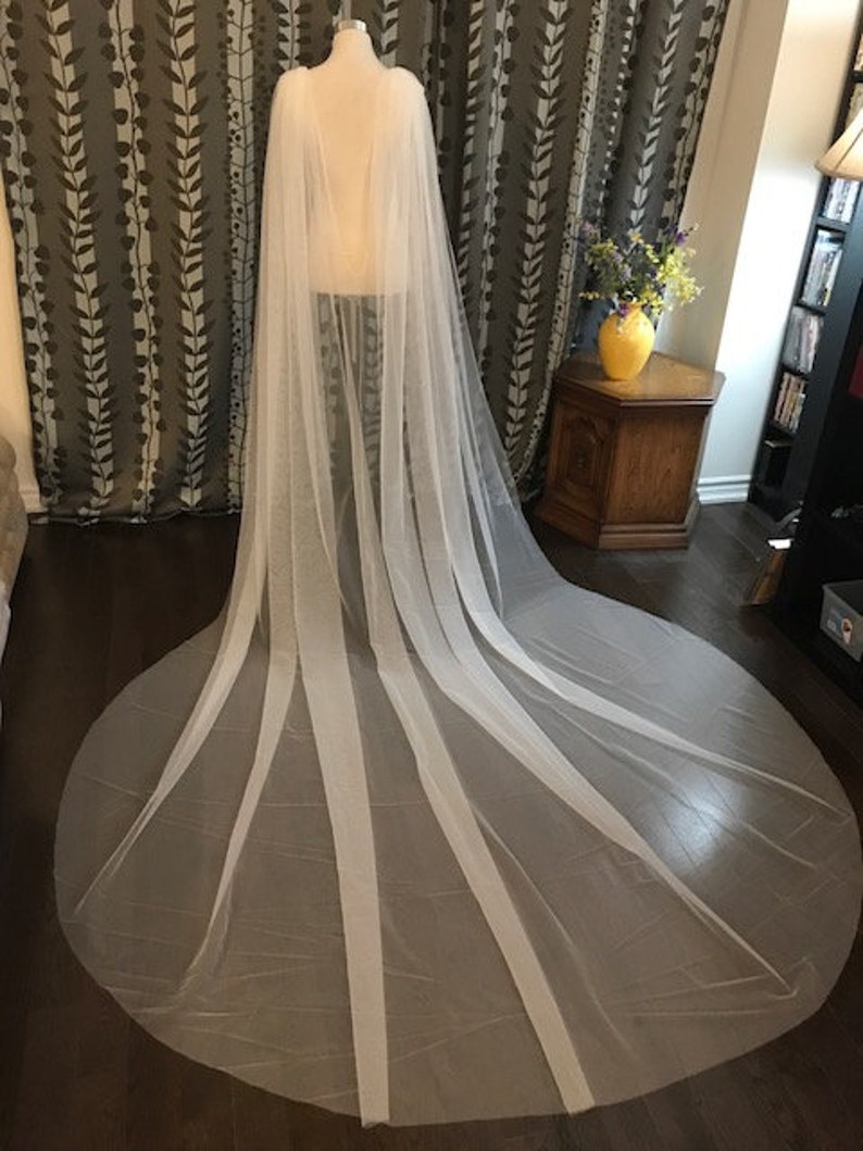 May include: A white tulle bridal veil with a long train. The veil is made of soft, sheer fabric and has a delicate, flowing design.