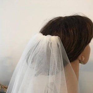 May include: A white single-tier bridal veil made of soft tulle, worn on a person's head.