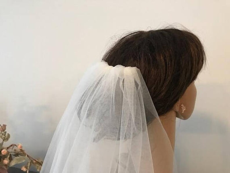 May include: A white single-tier bridal veil made of soft tulle, worn on a person's head.