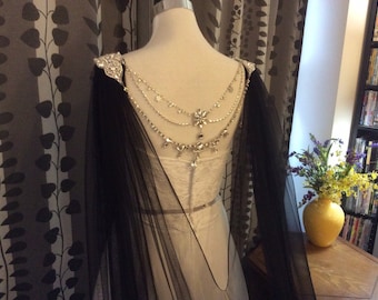 May include: A black sheer cape with a crystal and rhinestone embellishment on the back. The cape is draped over a white dress form.