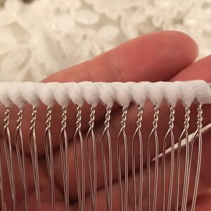 May include: White fabric trim with a row of silver metal loops. The loops are twisted and have a pointed end.