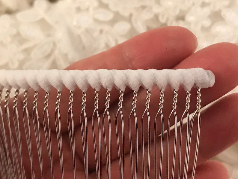 May include: White fabric trim with a row of silver metal loops. The loops are twisted and have a pointed end.