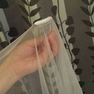 May include: A white bridal veil made of sheer, lightweight tulle fabric. The top of the veil is gathered and securely attached to a silver-toned metal hair comb with multiple teeth, designed to be inserted into hair for a secure hold.