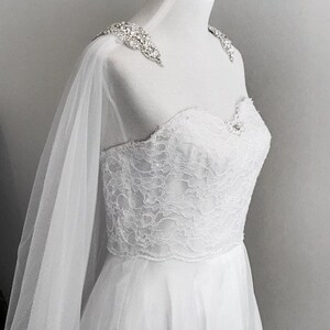May include: White lace wedding dress with a tulle overlay and a beaded embellishment on the shoulder straps.