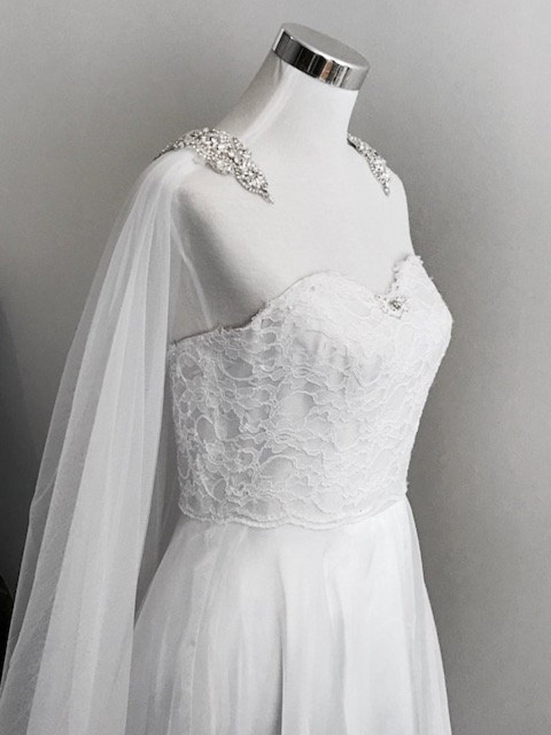 May include: White lace wedding dress with a tulle overlay and a beaded embellishment on the shoulder straps.