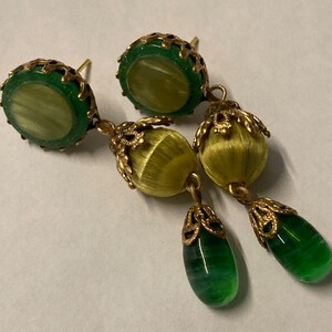 May include: A pair of green and gold earrings with a teardrop shaped green glass bead and a round yellow bead. The earrings have a filigree design.