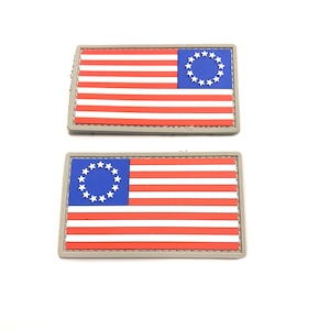 May include: Two gray fabric patches with a red, white, and blue American flag design. The flag has 13 stripes and a circle of 13 stars in the blue canton.