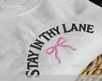 Peut inclure: Sweat-shirt blanc avec la phrase brodée "STAY IN THY LANE" en noir, arquée au-dessus d'un nœud rose. Disponible en tailles 12.7 cm, 15.2 cm, 17.8 cm et 20.3 cm.