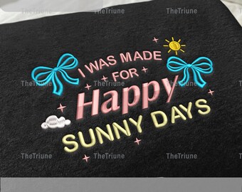 Peut inclure: Tissu noir brodé avec le texte "I WAS MADE FOR Happy SUNNY DAYS". Le motif comprend un soleil, des nuages, des nœuds et des étoiles. Le tissu mesure 12,7 à 20,3 cm.