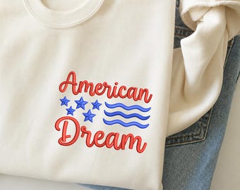 Peut inclure: Un sweat-shirt à col rond couleur crème avec le texte brodé en rouge American Dream. Le motif comprend cinq étoiles brodées bleues et trois lignes ondulées bleues. Le texte en haut indique STANDARD VERSION - 4 SIZES 5-6-7-8.