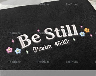 Peut inclure: Article brodé noir avec les mots "Be Still" et le verset biblique "Psaume 46:10". Le motif comprend des accents floraux et étoilés. Les dimensions de l'article sont de 12,7 à 20,3 cm.