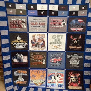 May include: A large, quilted blanket featuring a patchwork design of various Big Dogs t-shirts. The shirts display humorous slogans and graphics, including a dog with sunglasses and a car. The quilt has a blue and white striped border.