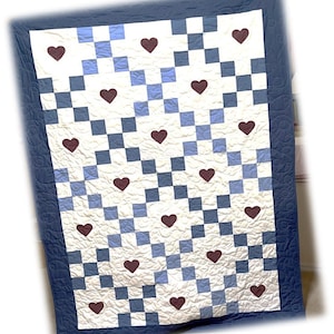 May include: A quilt with a blue border and a white and blue checkered pattern. The quilt is decorated with maroon hearts.