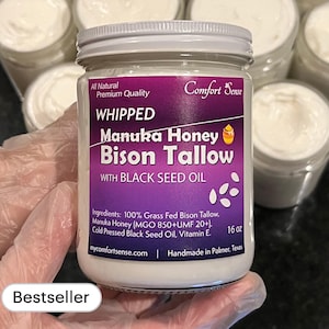 May include: A white jar of whipped Manuka honey and bison tallow body butter with black seed oil. The jar is labeled "Comfort Sense" and "Whipped Manuka Honey Bison Tallow with Black Seed Oil". The jar is 16 ounces and is handmade in Palmer, Texas.