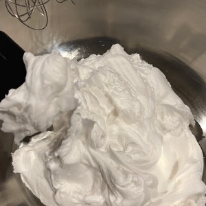 May include: A close-up of a white whipped cream frosting in a stainless steel mixing bowl.