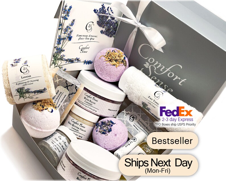 May include: A gray gift box filled with lavender-scented bath products, including bath bombs, bath salts, body butter, soap, and a loofah. The box is decorated with a white ribbon and a tag that says "Comfort Sense".