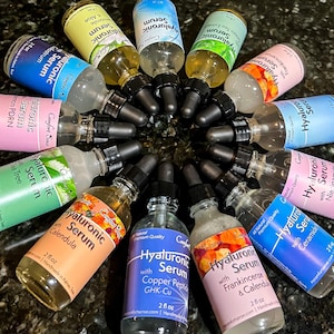 May include: A circular arrangement of twelve clear glass dropper bottles containing Hyaluronic Serum. Each bottle features a colored label with specific ingredient names like Calendula, Niacinamide, and Copper Peptide, all marked as 2 fl oz.