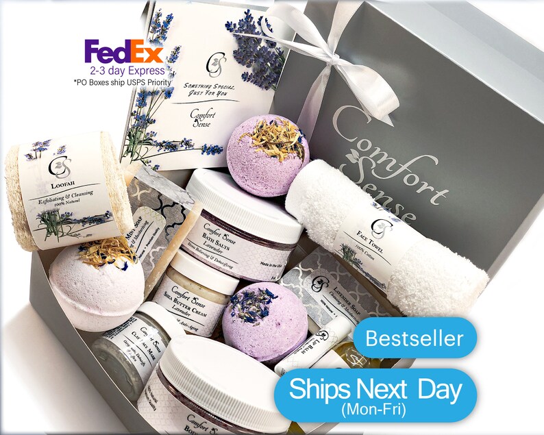 May include: A gray gift box filled with lavender-scented bath products, including bath bombs, bath salts, body butter, soap, and a loofah. The box also includes a white face towel. The box is labeled "Comfort Sense" and "Bestseller".