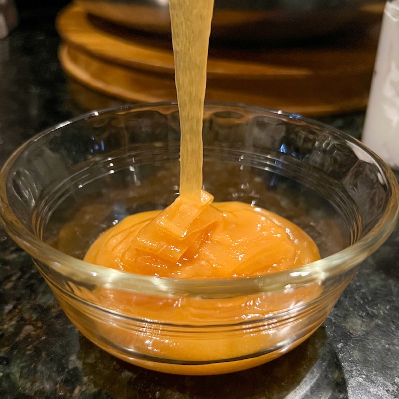 May include: A clear glass bowl filled with a bright orange, thick, and viscous liquid. The liquid is being poured from a container above the bowl.