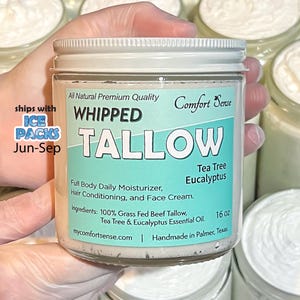 May include: A clear glass jar with a white lid, labeled "WHIPPED TALLOW" with "Tea Tree Eucalyptus" and "16 oz" on the label. The jar is held in a gloved hand, with other jars in the background. The label also states "Full Body Daily Moisturizer, Hair Conditioning, and Face Cream."