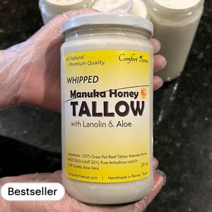 May include: A glass jar of whipped Manuka honey tallow with lanolin and aloe. The jar is labeled "Comfort Sense" and "All Natural Premium Quality". The label also states "Ingredients: 100% Grass Fed Beef Tallow, Manuka Honey MGO 850+UMF 20+, Pure Anhydrous Lanolin USP Grade, Aloe Vera. 24 oz. Mycomfortsense.com Handmade in Palmer, Texas."
