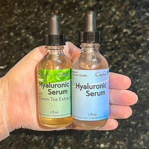 May include: Two clear glass dropper bottles containing 2 fl oz of Hyaluronic Serum. The left bottle features a green label with the text Hyaluronic Serum with Green Tea Extract. The right bottle has a blue label with the text Hyaluronic Serum.