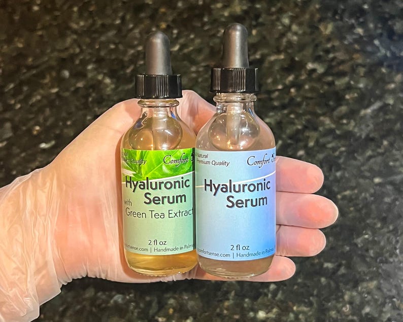 May include: Two clear glass dropper bottles containing 2 fl oz of Hyaluronic Serum. The left bottle features a green label with the text Hyaluronic Serum with Green Tea Extract. The right bottle has a blue label with the text Hyaluronic Serum.