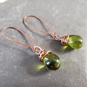 May include: A pair of copper wire earrings with green glass teardrop beads. The earrings are simple and elegant.