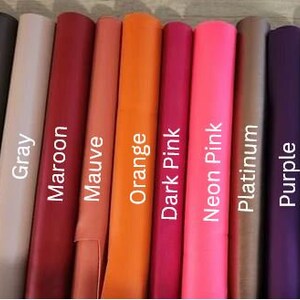 Op de afbeelding: Een selectie van 12 lederen swatches in verschillende kleuren, waaronder goud, donkergrijs, grijs, bordeauxrood, mauve, oranje, donkerroze, neonroze, platina, paars, donkerpaars en rood.