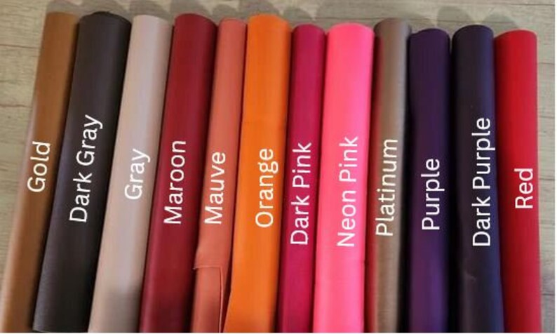 Op de afbeelding: Een selectie van 12 lederen swatches in verschillende kleuren, waaronder goud, donkergrijs, grijs, bordeauxrood, mauve, oranje, donkerroze, neonroze, platina, paars, donkerpaars en rood.