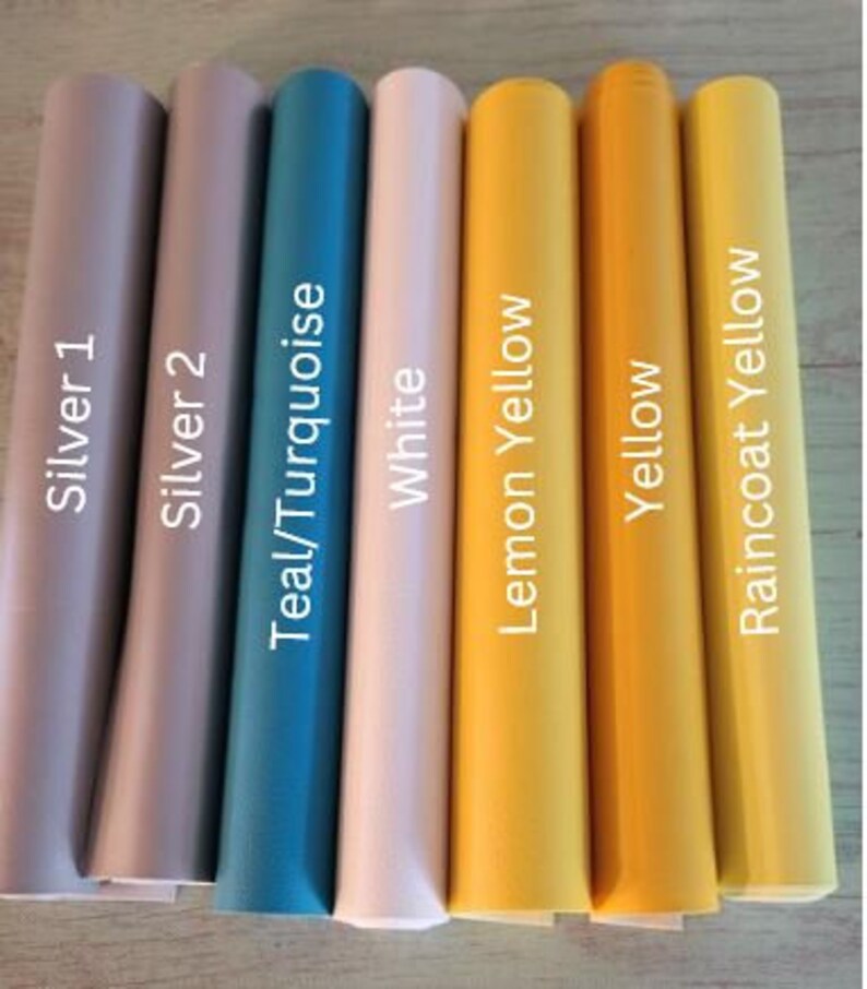 Op de afbeelding: Acht rollen vinyl plakband in verschillende kleuren, waaronder zilver, teal, wit, citroengeel, geel en regenjasgeel. De rollen zijn gelabeld met hun respectievelijke kleuren.