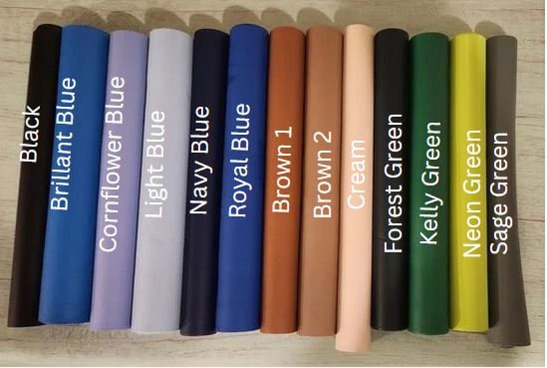 Op de afbeelding: Een verzameling van 13 stofstalen in verschillende kleuren, waaronder zwart, blauw, bruin, cr&egrave;me en groen. De stalen zijn horizontaal gerangschikt en gelabeld met hun respectievelijke kleuren.