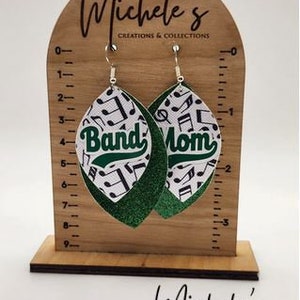 Op de afbeelding: Een paar groene en witte oorhangers met een muzieknootpatroon en de woorden "Band Mom" erop.