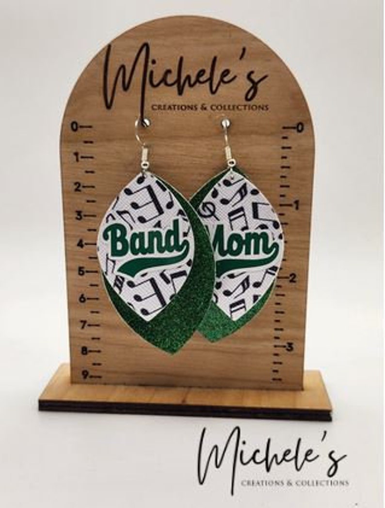 Op de afbeelding: Een paar groene en witte oorhangers met een muzieknootpatroon en de woorden "Band Mom" erop.