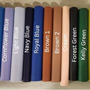 Op de afbeelding: Een selectie van 13 stofstalen in verschillende kleuren, waaronder zwart, blauw, bruin, cr&egrave;me en groen. De stalen zijn in een rij van links naar rechts gerangschikt, met de kleurennamen afgedrukt onder elk staal.