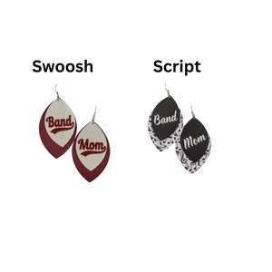Op de afbeelding: Twee paar hangende oorbellen. Het eerste paar is bordeauxrood met witte en gouden letters die "Band" en "Mom" zeggen in een schrijfletter. Het tweede paar is zwart met witte en zilveren letters die "Band" en "Mom" zeggen in een schrijfletter. De oorbellen zijn op een witte achtergrond.
