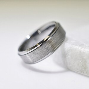 May include: A silver wedding band with a brushed finish and a polished edge.