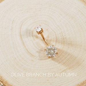 May include: Gold belly button ring with two clear round cubic zirconia stones.