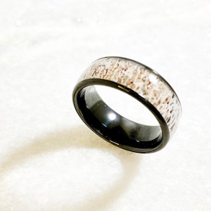 May include: A black ceramic ring with a white antler inlay. The ring is polished and has a smooth finish.