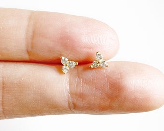 May include: A pair of gold earrings with small, clear cubic zirconia stones set in a clover shape.
