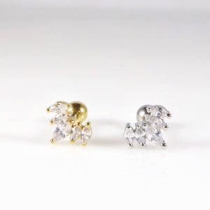May include: Two silver and gold ear cartilage earrings with a cluster of clear marquise-shaped stones. The earrings are designed to be worn on the upper cartilage of the ear.