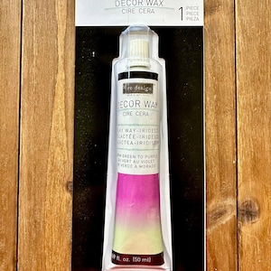 May include: A tube of Re-Design Decor Wax in Milky Way-Iridescent, packaged on a black and white cardboard backing. The tube features a gradient color transition from purple to light green, with text indicating a 1.69 fl. oz. (50 ml) volume.