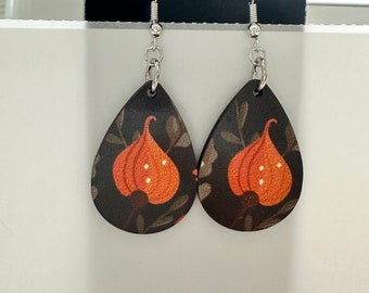 May include: A pair of dangle earrings with a dark brown background and orange floral pattern. The earrings are made of wood and have silver hooks.